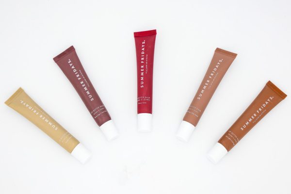 Five lip balm tubes in various colors that say “SUMMER FRIDAYS” in white font arranged on their side in an arch formation. 