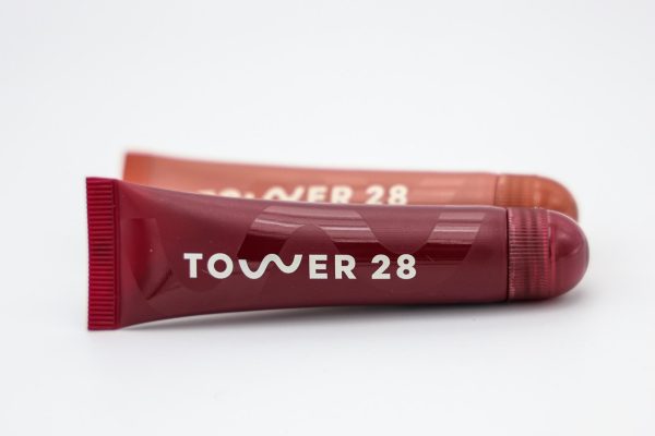 Two lip balms with the words "TOWER 28" displayed horizontally, one is orange and the other is dark red.