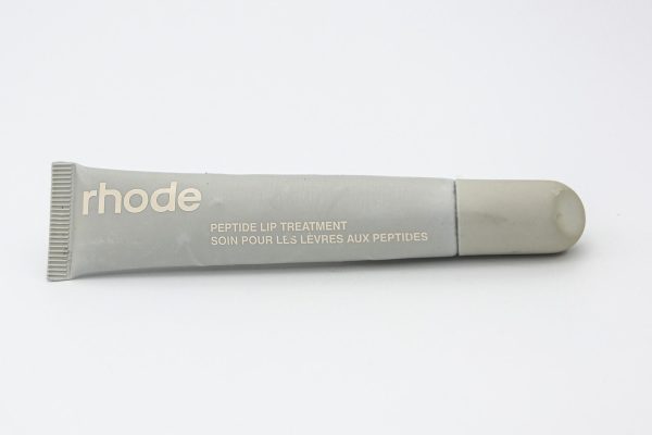 Gray tube of lip gloss displayed horizontally with “RHODE” in white font on the side.