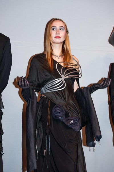 Model wearing a draped black dress with sculpted metal accents.