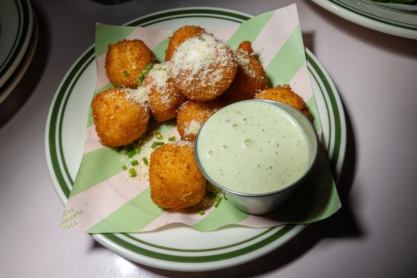 A plate with fried balls of dough and a cup of light green sauce.