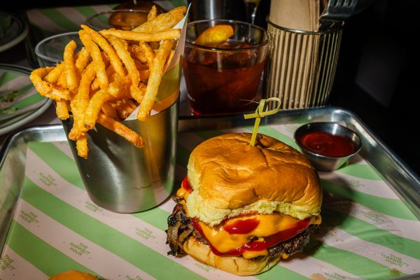 A tray with a cup of french fries, a burger with a toothpick skewered through the center and a cup of ketchup.
