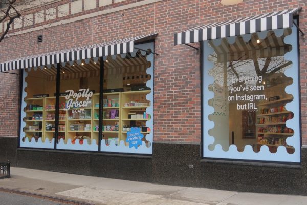 A storefront with text that reads “Pop Up Grocer & CAFE.”