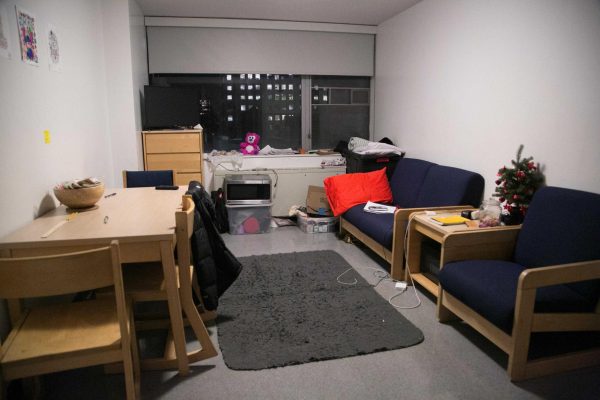 A single dorm room with one bed, one couch, a chair and a dresser. 