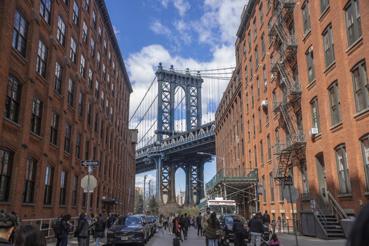 Line of red buildings on a cobblestone street with a view of the Manhattan Bridge in the background.