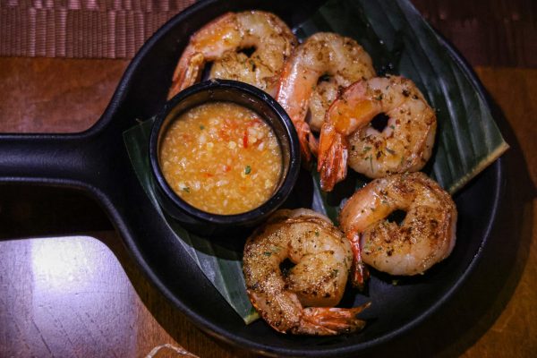 An iron skillet with five shrimp and an orange sauce in a small bowl. 