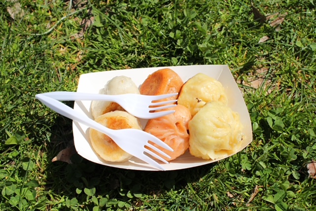 A paper tray on grass with six bao buns and two forks on it.