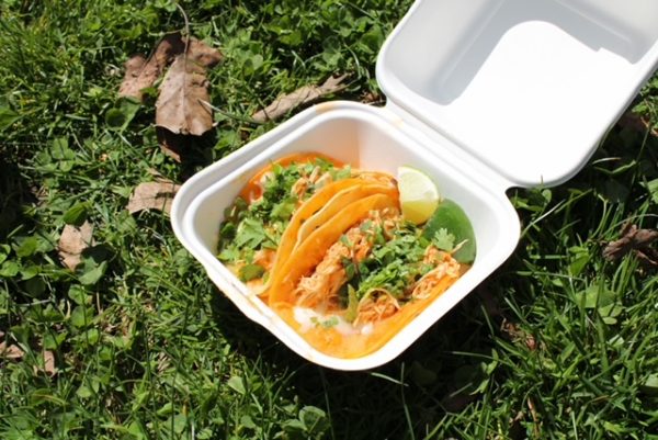 A white container holding tacos with chicken and cilantro in them sitting on grass. 