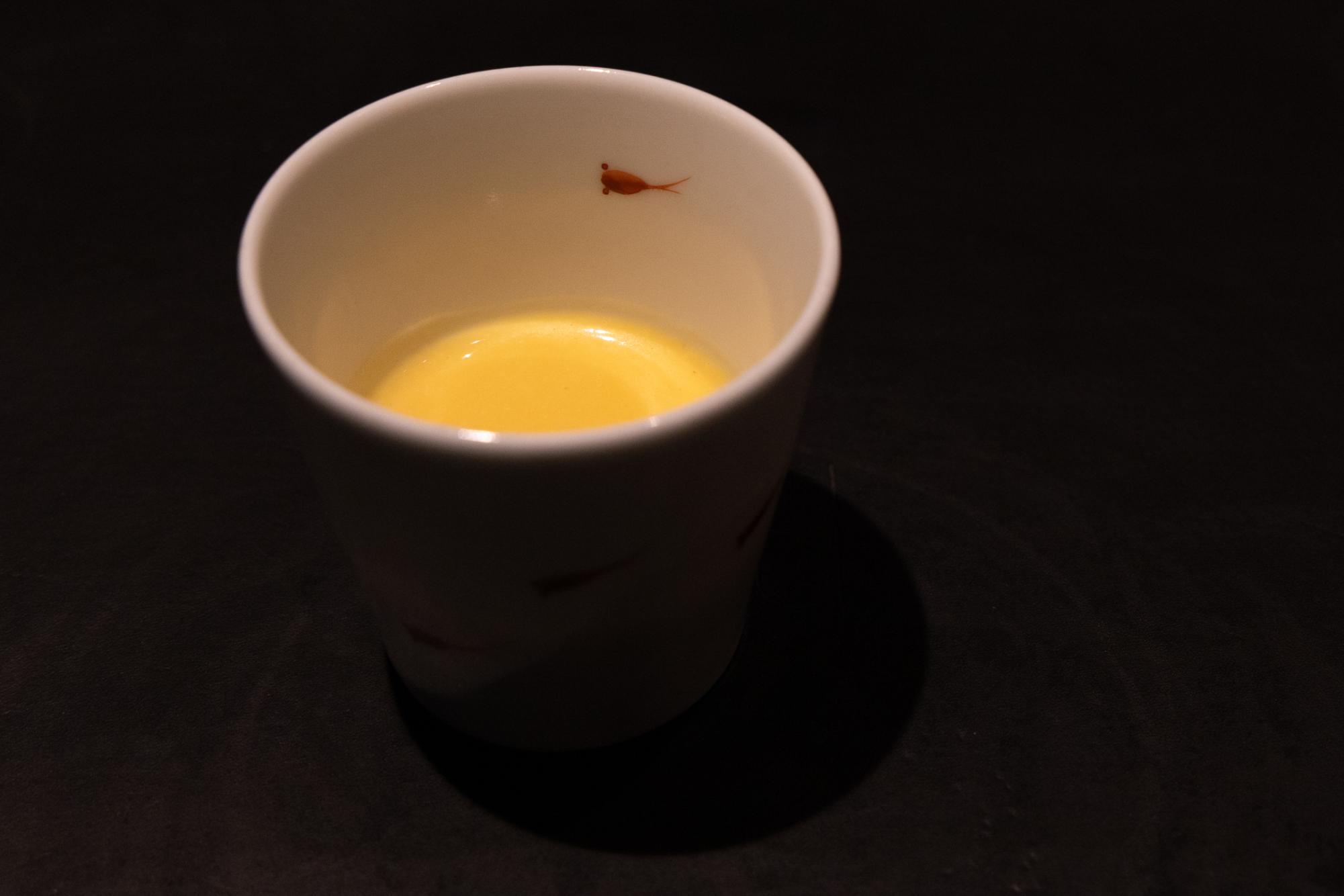 A white cup with yellow soup.