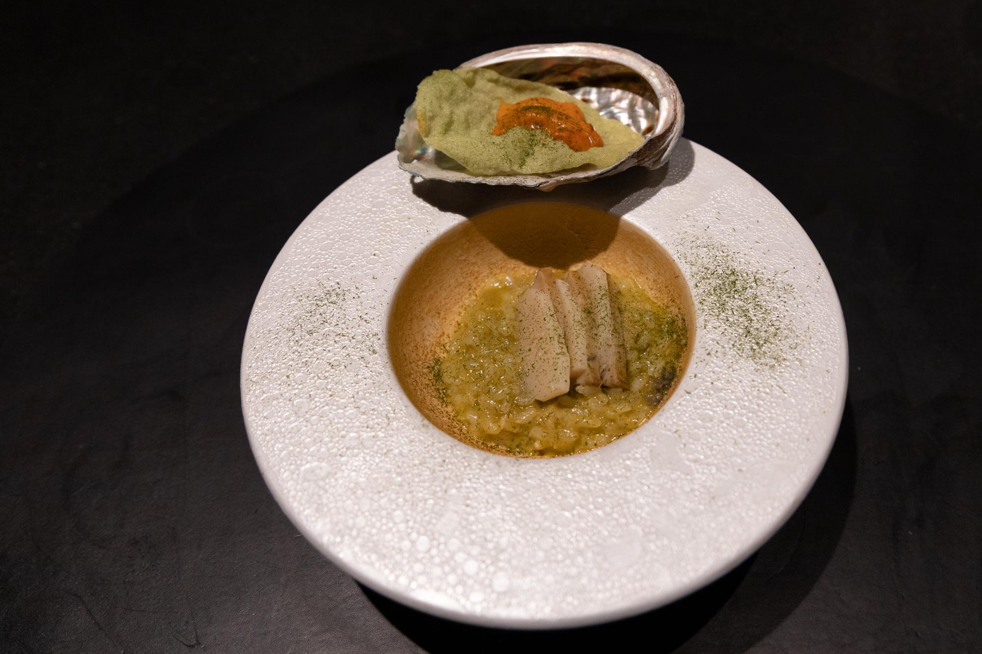 A white bowl containing risotto topped with abalone.