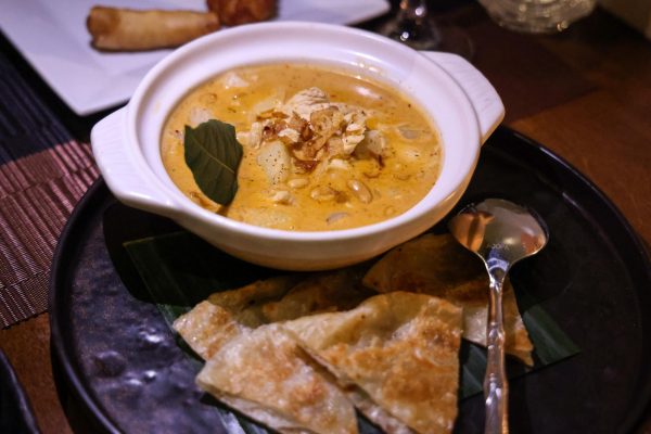 A yellow curry with salted peanuts and potatoes in a white bowl. There are five pieces of flatbread next to the bowl. 
