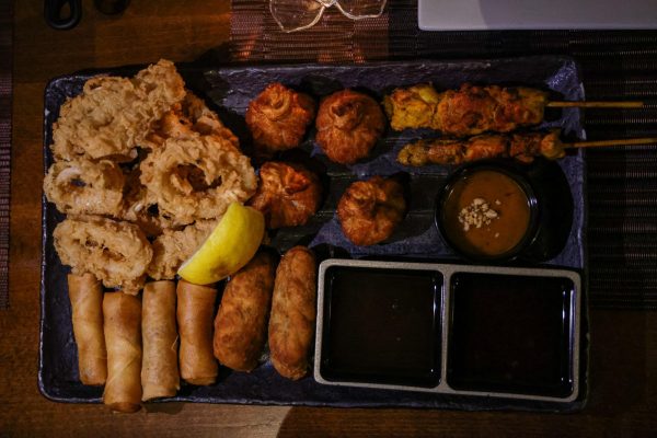 A tray with fried calamari, spring rolls, fried dumplings, chicken satay, two different sauces and curry puffs.