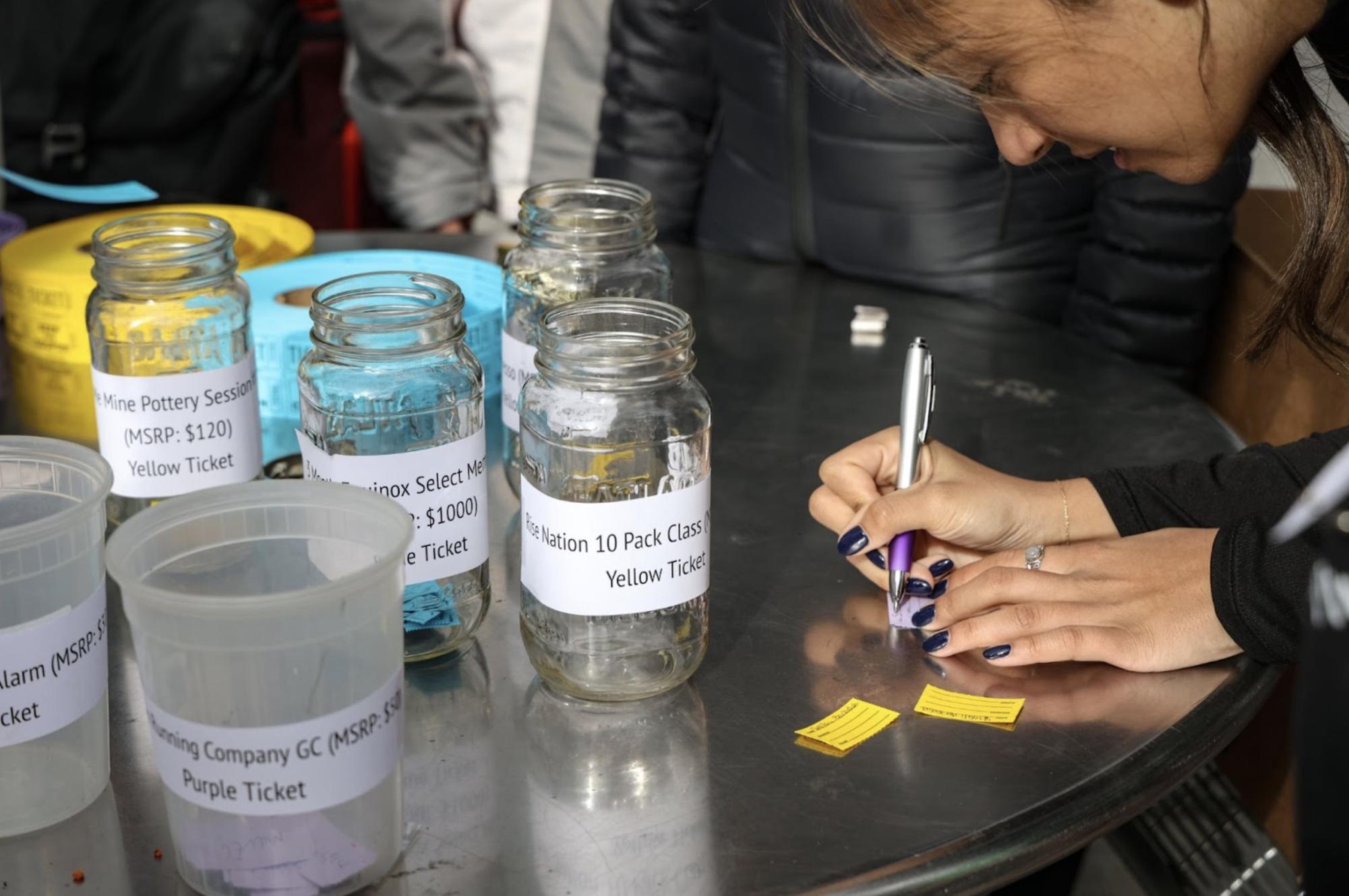A participant writes her name on a raffle ticket on a table full of mason jars with prizes written on them.
