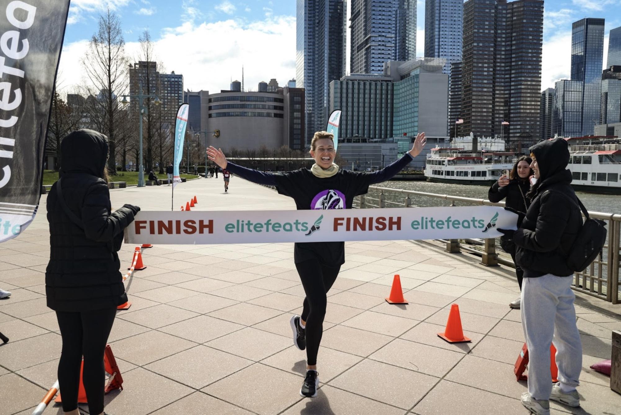 A woman raises her hands triumphantly as she crosses the finish line.