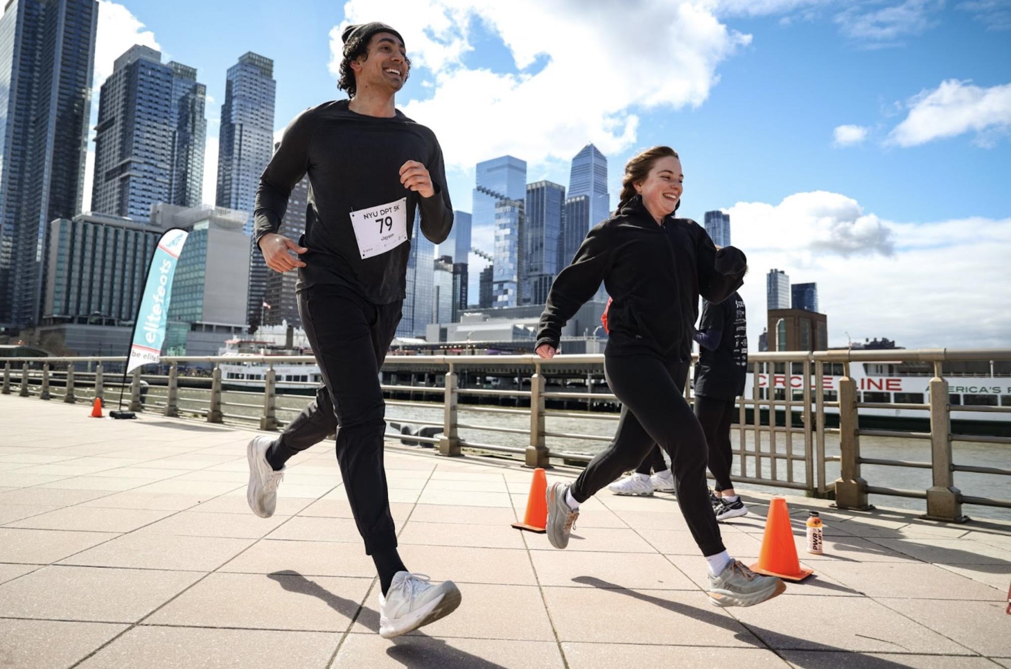 Two people run in front of the New York City skyline smiling.