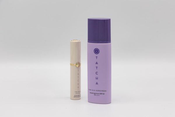 A beige Tatcha lip tint with spf next to a purple Tatcha sunscreen stick.