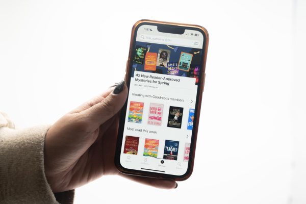 A hand holds a phone with a virtual book library on the screen.