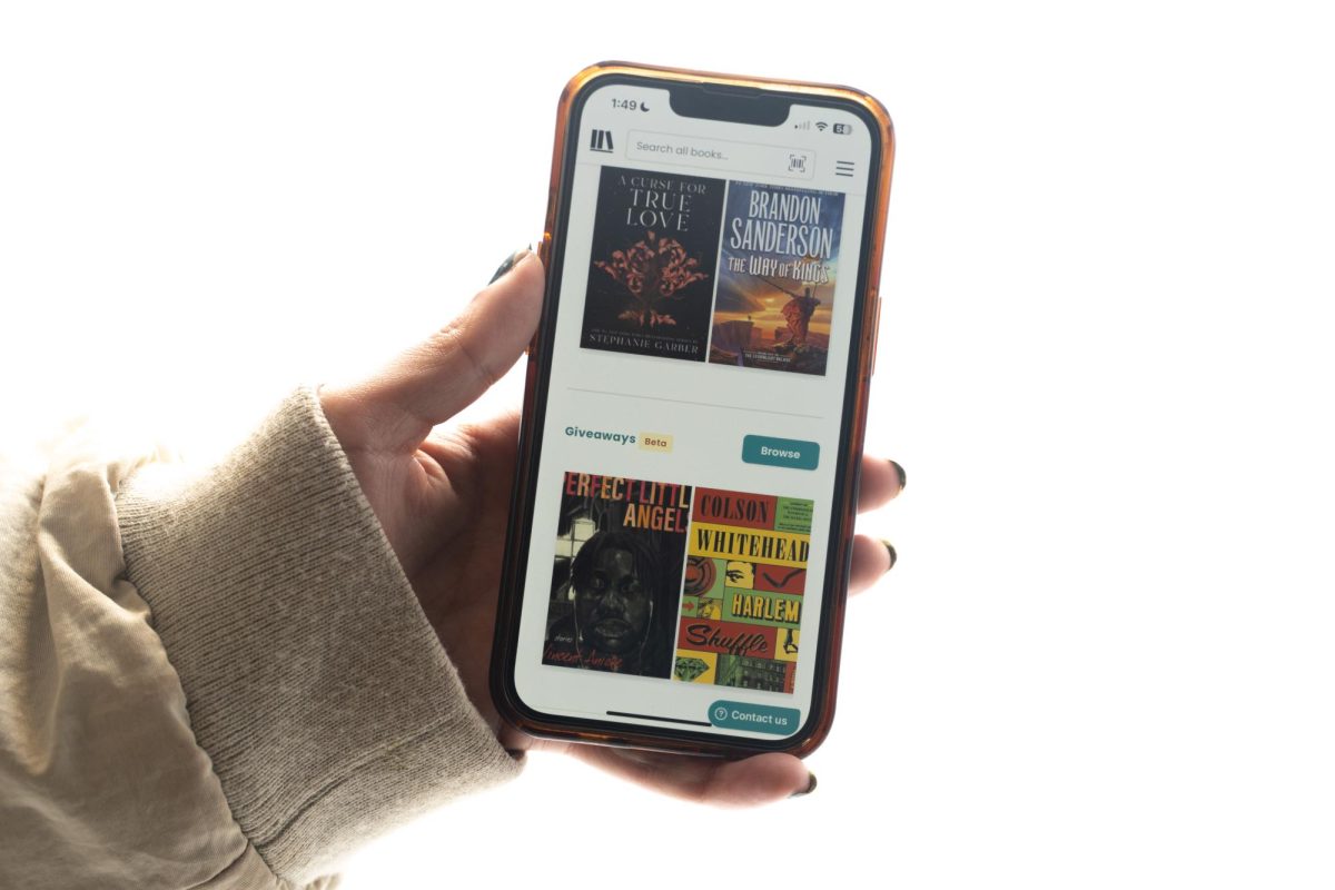 A hand holds a phone with images of four books on the screen.