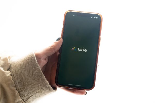 A hand holds a phone with the word “Fable” on the screen.