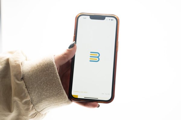 A hand holds a phone with the letter “B” on the screen.
