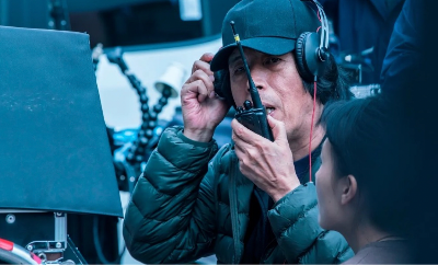 A man with headphones speaking into a walkie talkie on a film set.