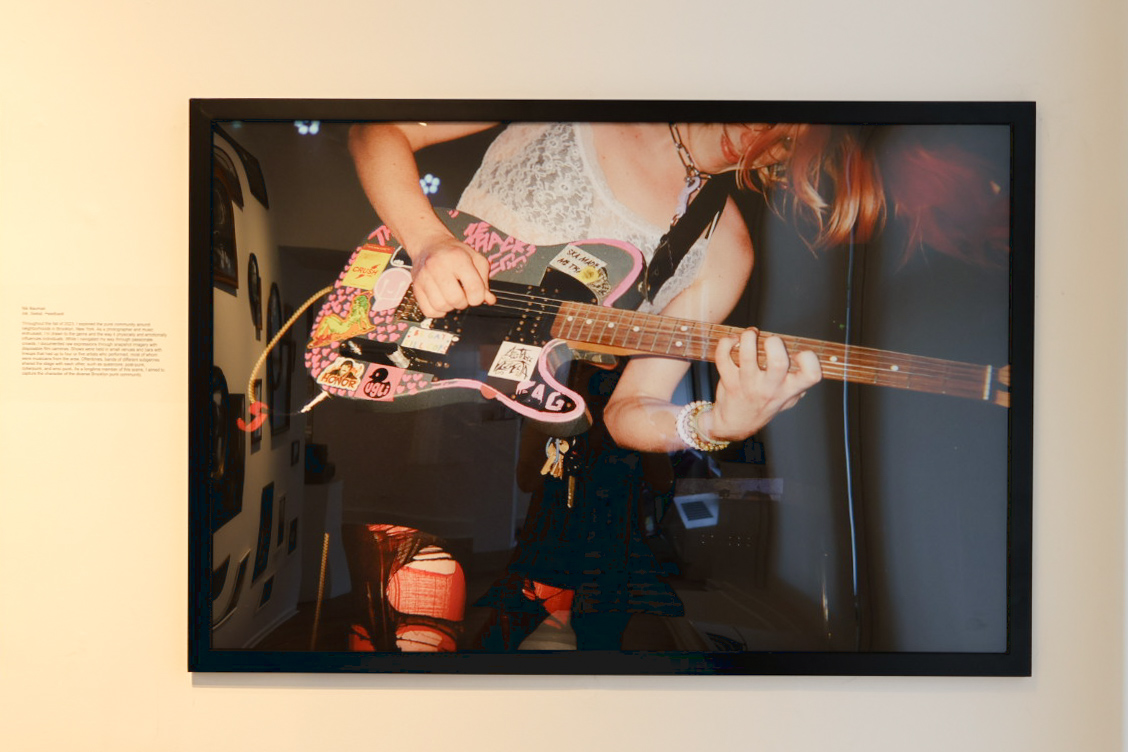 Photo of a person playing a pink-and-black electric guitar on display in a gallery.