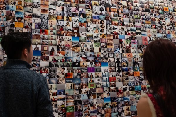 Two people look at a wall filled with a collage of color pictures.