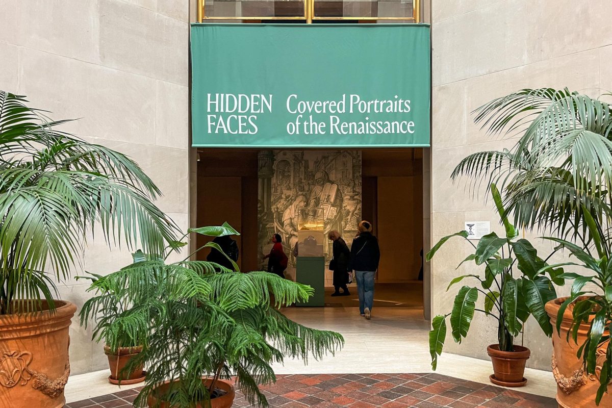 An entrance to an exhibit is surrounded by potted plants. Above the entrance are the words “Hidden Faces: Covered Portraits of the Renaissance.”