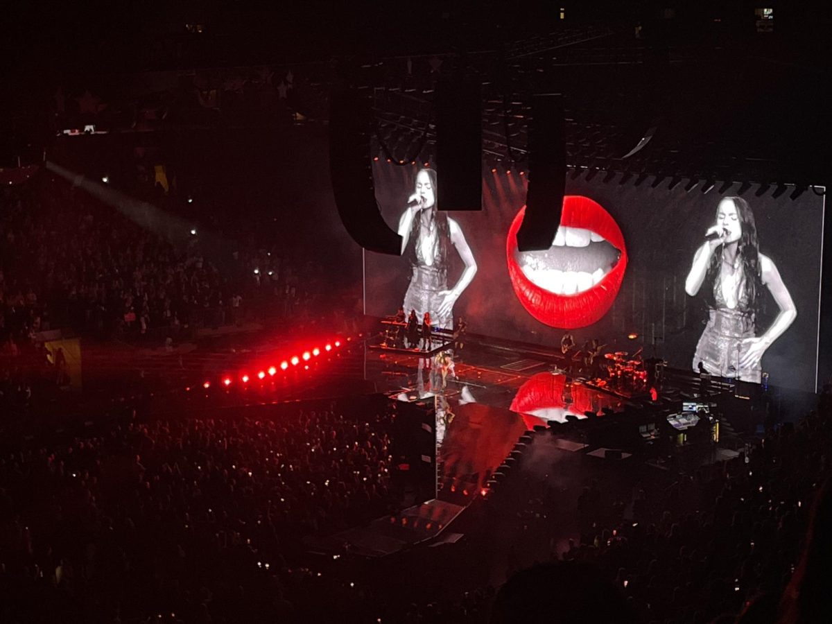 Photo+of+a+large+stage+displaying+red+lips+signing+alongside+a+stage+cam+of+a+woman+signing+into+a+microphone+on+either+side.