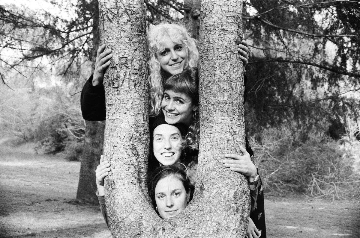 A+black+and+white+image+of+four+smiling+women+poking+their+head+through+a+tree.