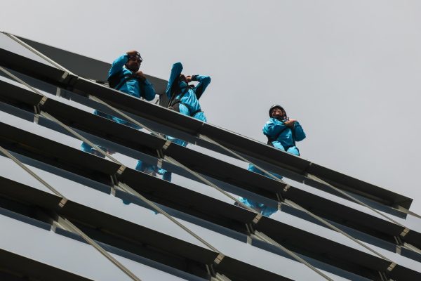Three people in blue jumpsuits and harness gear stand atop a tall structure.