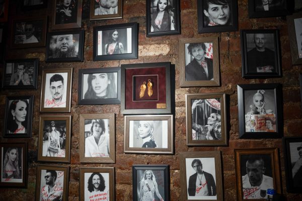 A black-and-white wall of celebrity photos with a red frame with two gold shoe-shaped charms at the center.