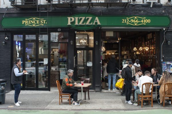 The exterior of Prince Street Pizza, with a green sign that says "Prince Street Pizza" and their phone number and people sitting at tables outside the restaurant.