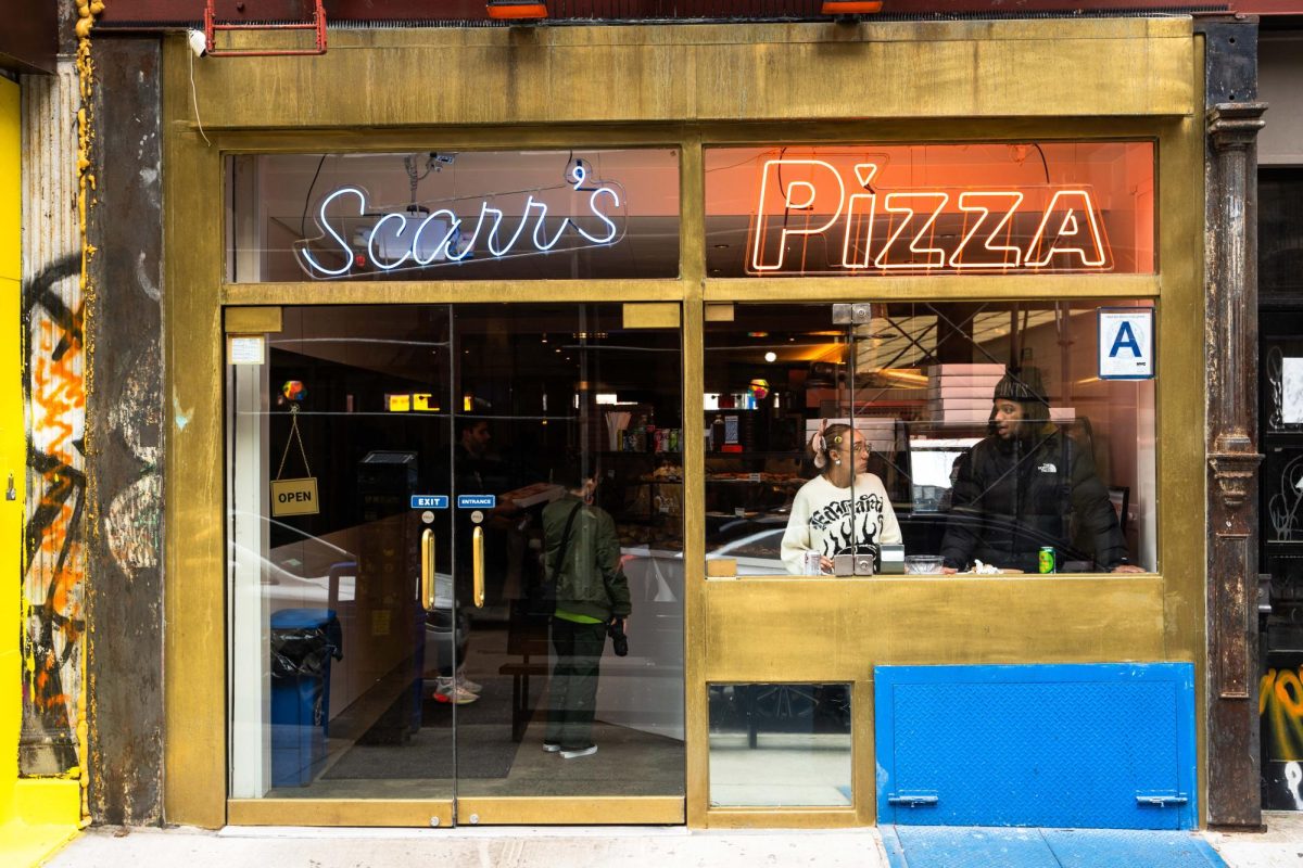 The exterior of Scarr’s Pizza, with a sign that says “Scarr’s Pizza,” and two people inside.