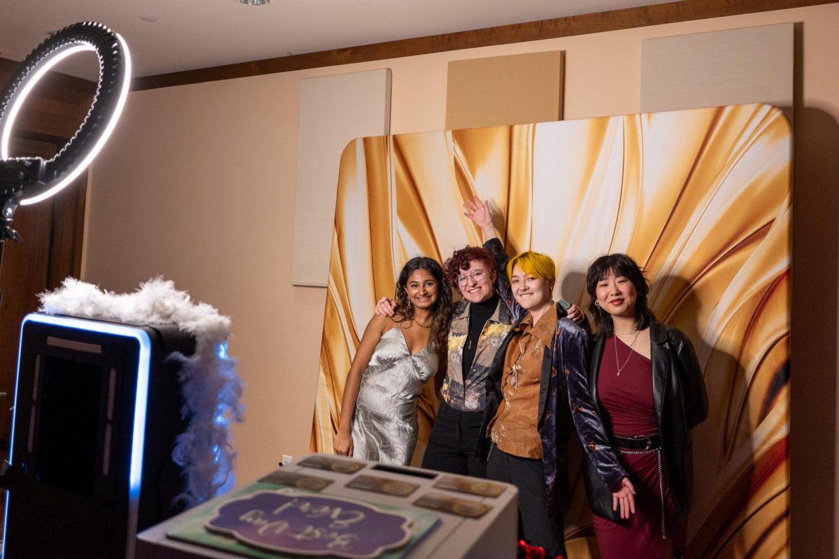 Four people in formal wear pose for a photo in front of an orange and white backdrop.