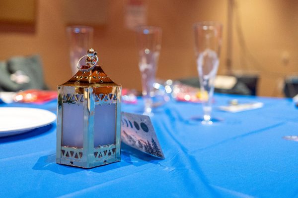 A place setting lantern and paper card on a blue tablecloth with empty glasses scattered around.