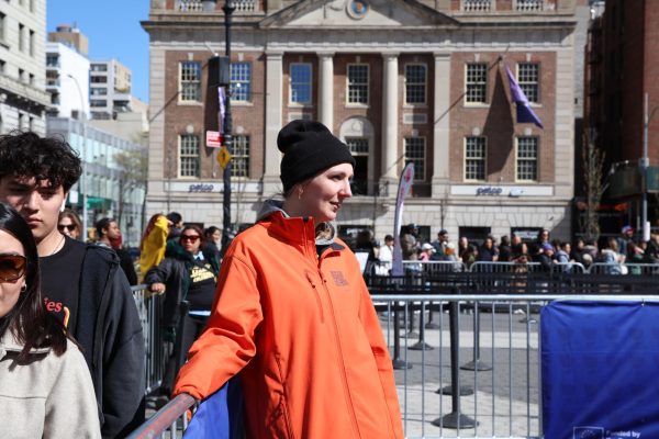 A woman in an orange jacket and black beanie leans against a barricade. Hundreds of people behind her line up to enter the garden.