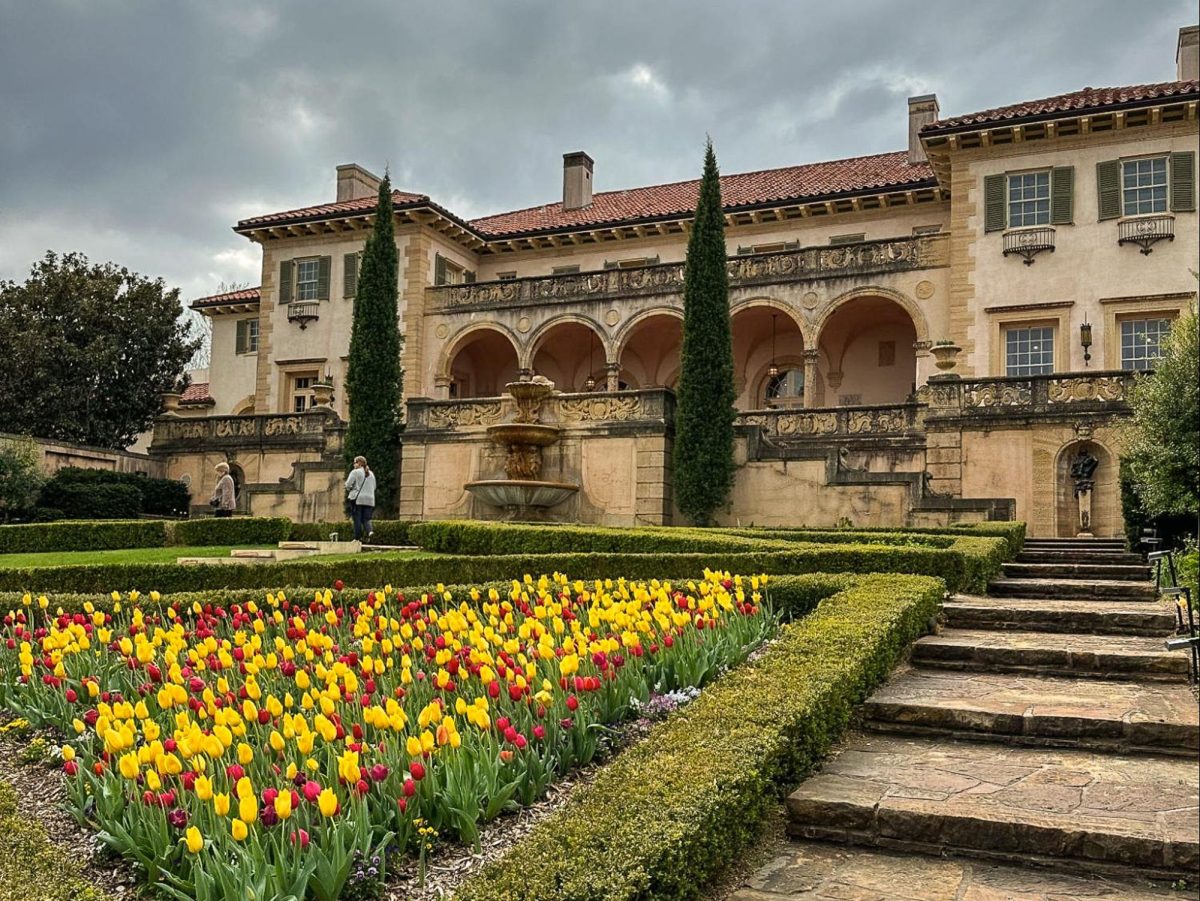 A yellow building with green trees in the front and a yellow and red tulip garden in the front of the Philbrook Museum of Art