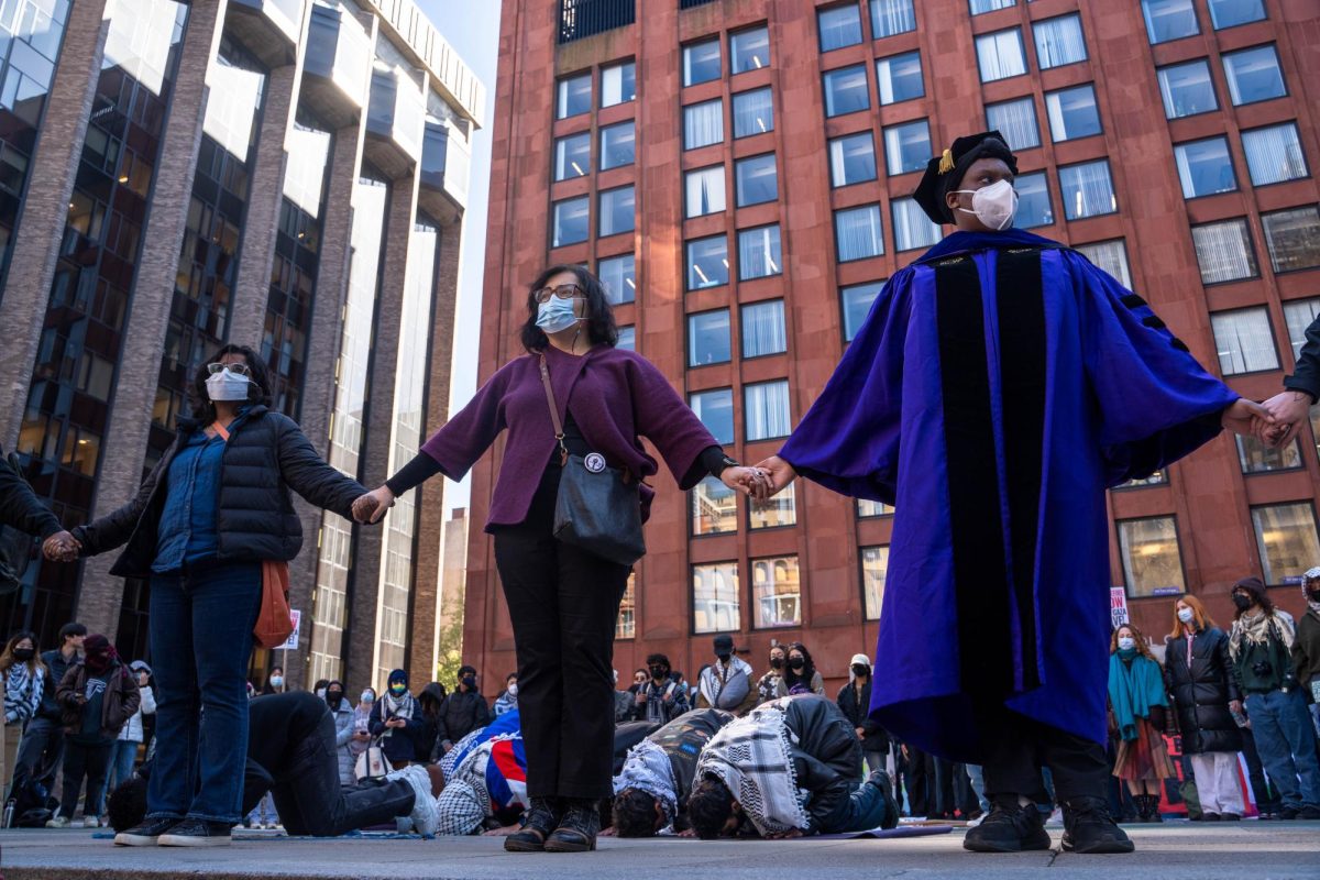Three faculty members with face masks hold hands in front of protesters that are praying.