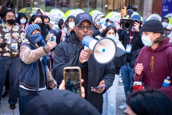 A man with a megaphone address a large crowd.