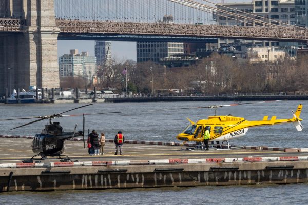 Two helicopters, one yellow and the other black, sit on a helipad on the water.