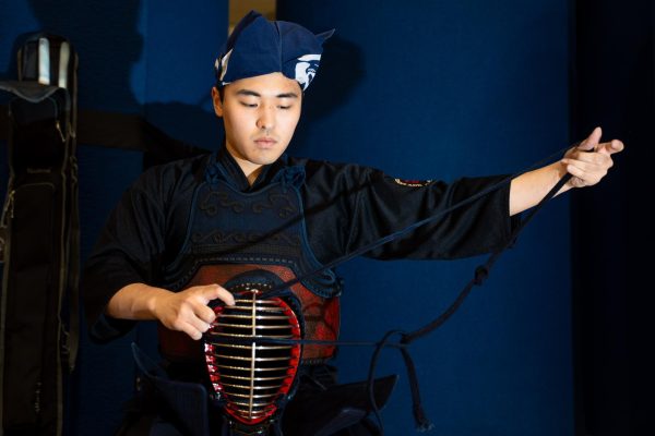A man in traditional kendo wear, holding a string on the garment in front of himself.
