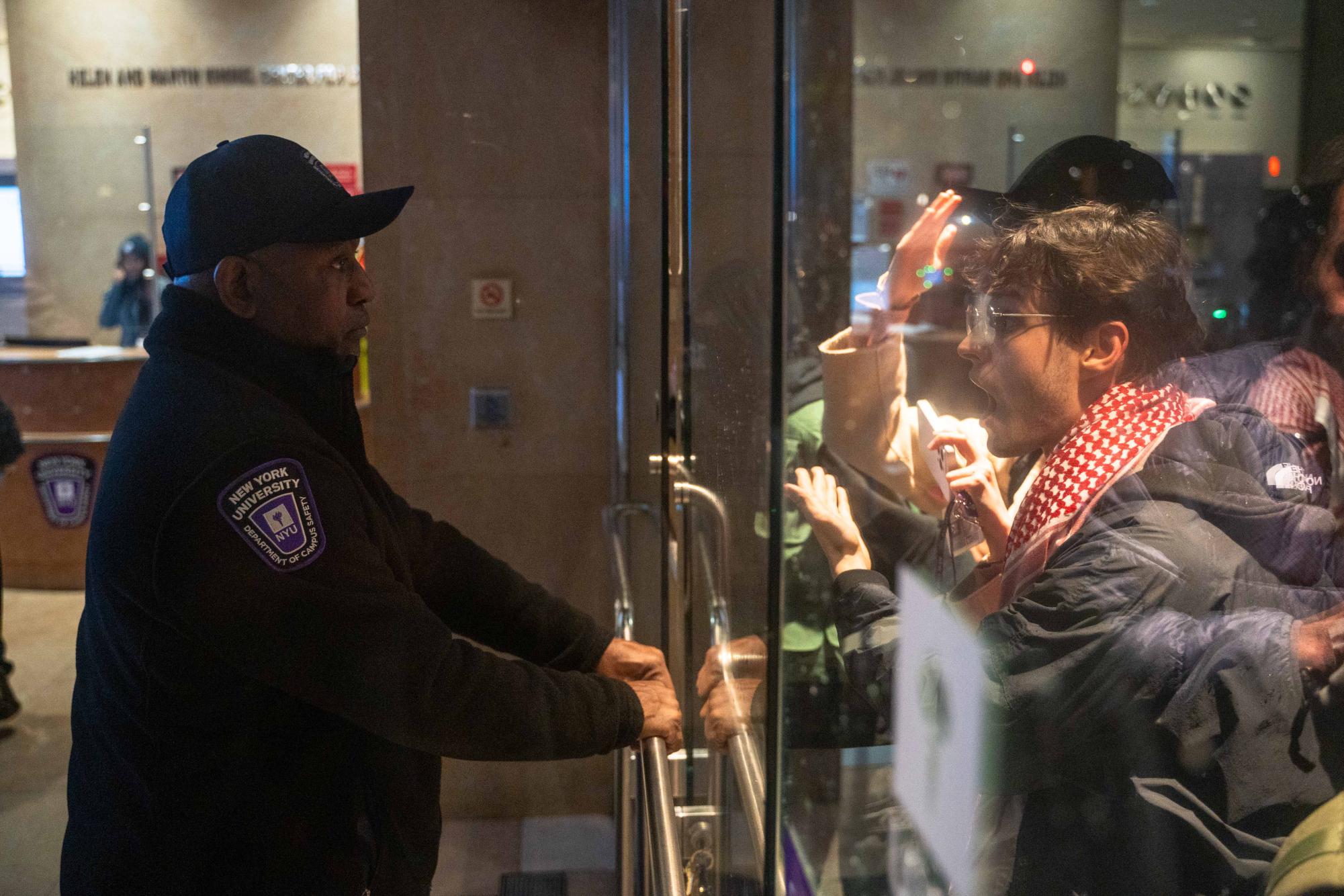 A Campus Safety officer holds a door closed as protesters try to enter the Kimmel Center for University Life.