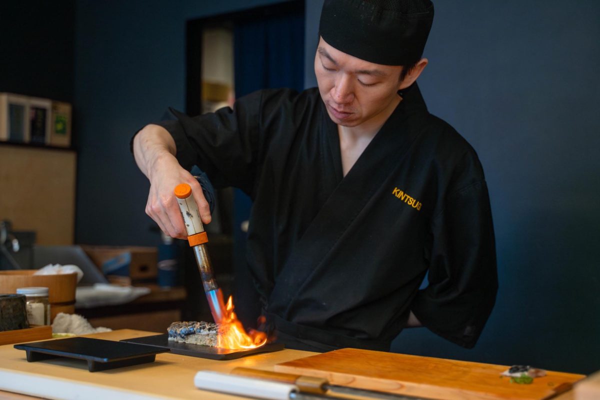 A man uses a blowtorch on a piece of sushi.