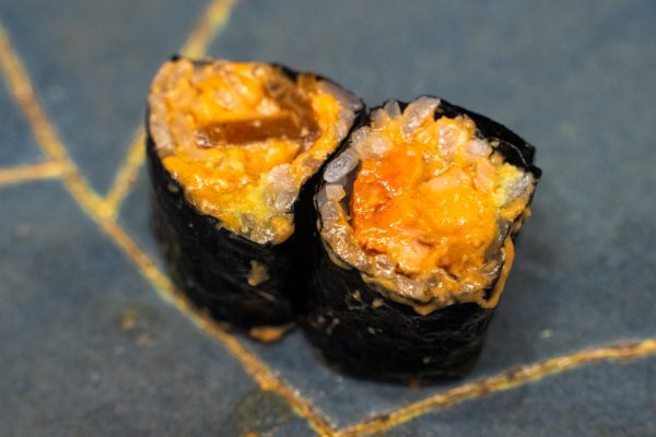 Two sushi rolls with rice and monkfish liver covered in a yellow sauce.