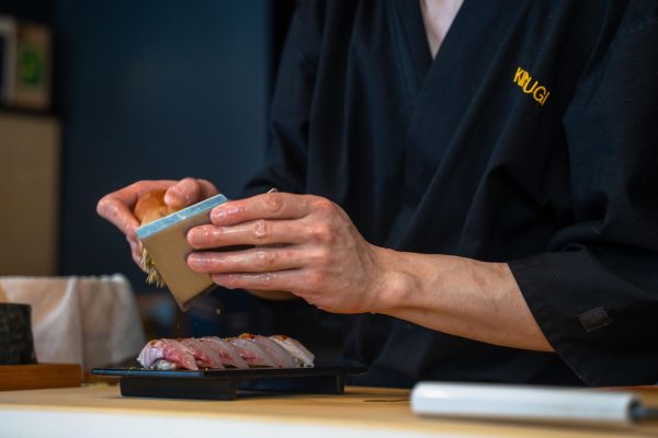 Man garnishing a sushi roll with a brush tool.