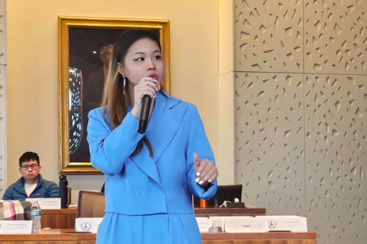 A woman in a blue suit speaks into a microphone.