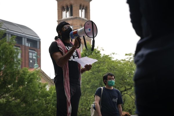 A person holding a megaphone leads chants in front of a crowd.