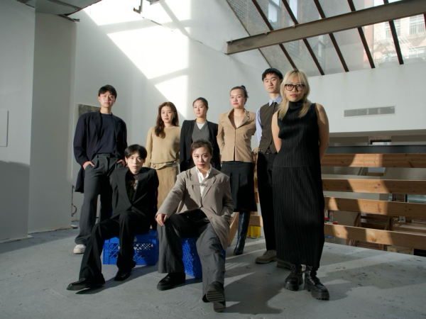 Eight people pose for a camera in a warehouse, six standing in the back and two siting in the front.