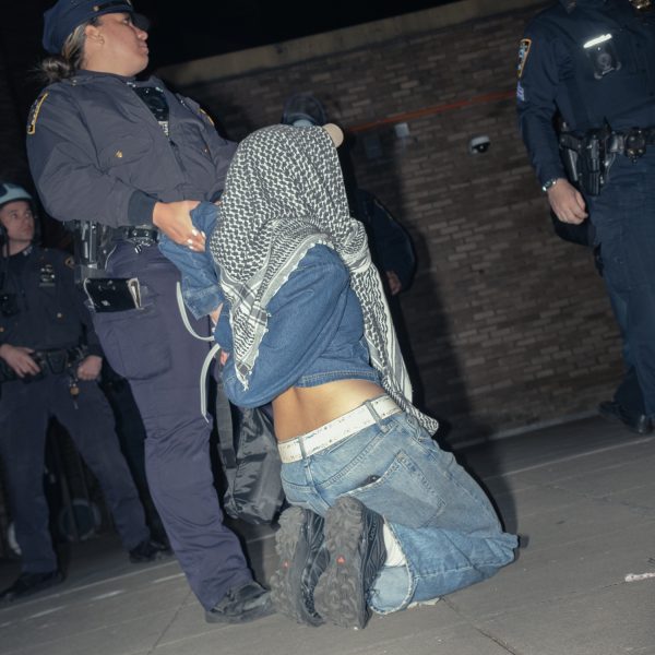 A protester arrested with a zip tie kneels on the floor as an N.Y.P.D. officer drags them across the ground.